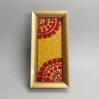 Decorative mosaic tray with red and yellow patterns in a gold frame on a textured surface.