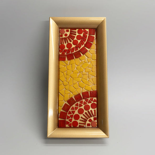 Decorative mosaic tray with red and yellow patterns in a gold frame on a textured surface.